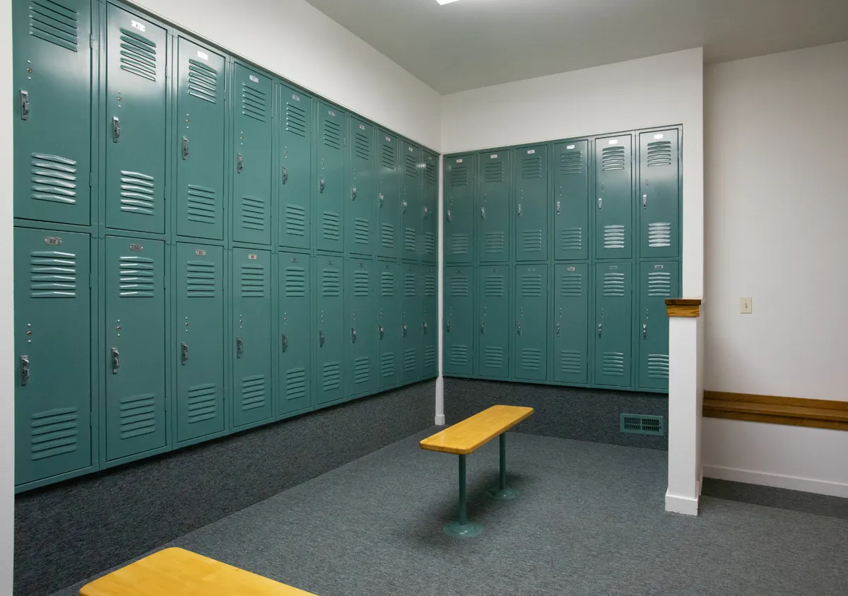 A practical ski locker room featuring a row of green lockers and a sturdy wooden bench. The space is functional, designed for storing gear and providing a place to change before or after hitting the slopes. Clean lines and simple design reinforce the focus on convenience and efficiency.