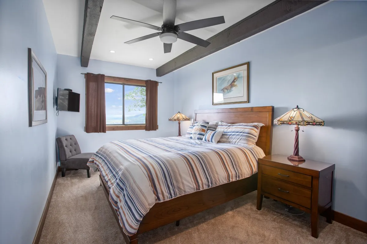 A tranquil and comfortable bedroom featuring a plush bed topped with fresh linens, soft lighting from bedside lamps, and a window allowing natural light to stream in. Subtle artwork adorns the wall, enhancing the serene ambiance ideal for restful nights.