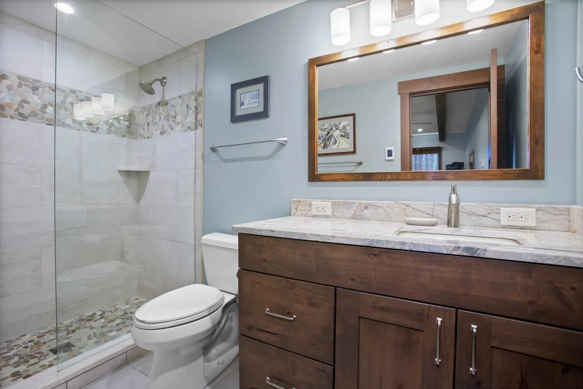 A modern, inviting bathroom with a glass shower enclosure, sleek vanity with countertop, well-lit mirror, and tasteful wall art. The space feels fresh and relaxing, ideal for self-care routines.