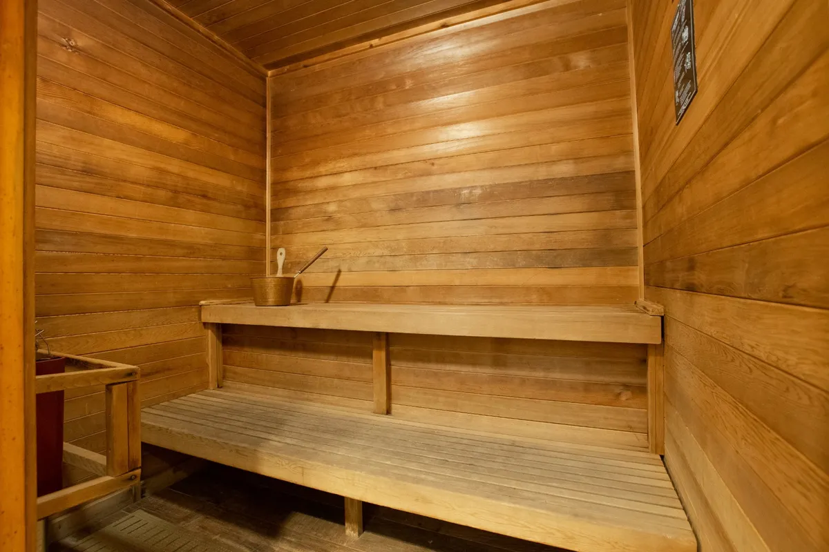 A calming interior sauna featuring wooden benches, wooden walls, and wellness accessories like a bucket and ladle. The space exudes a tranquil, spa-like environment perfect for post-workout relaxation and wellness treatments.