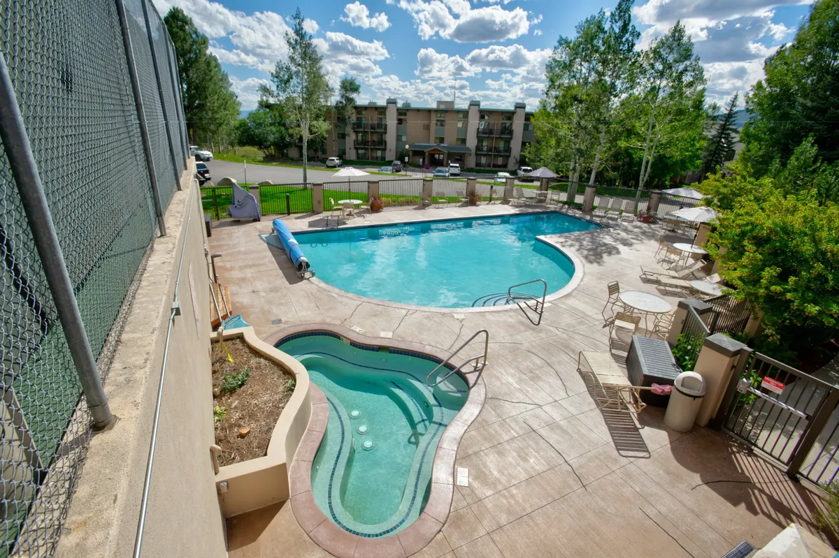 An inviting outdoor pool and hot tub occupy the foreground, surrounded by lounge chairs and lush greenery. The setting is both relaxing and social, ideal for unwinding after a day on the slopes.