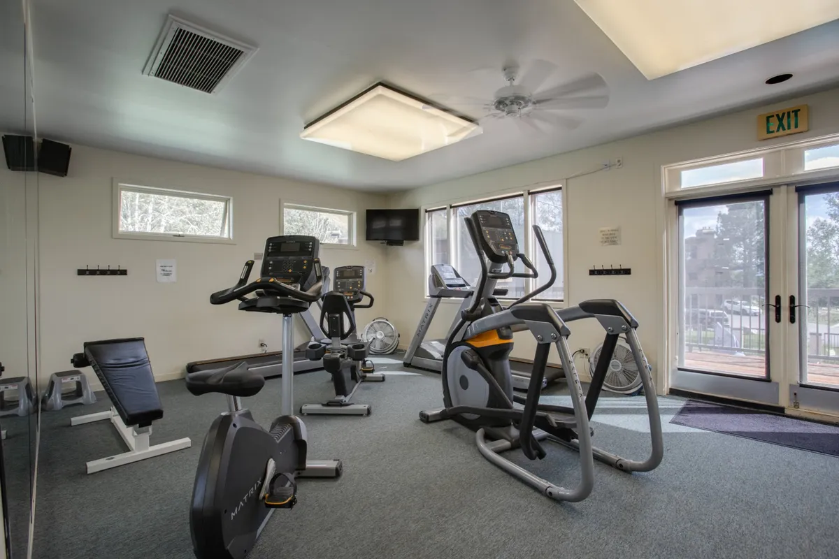 An interior fitness center filled with modern exercise equipment, large windows letting in natural light, and mirrored walls. The space feels energetic and motivating, ideal for workouts, group fitness classes, or personal training sessions.