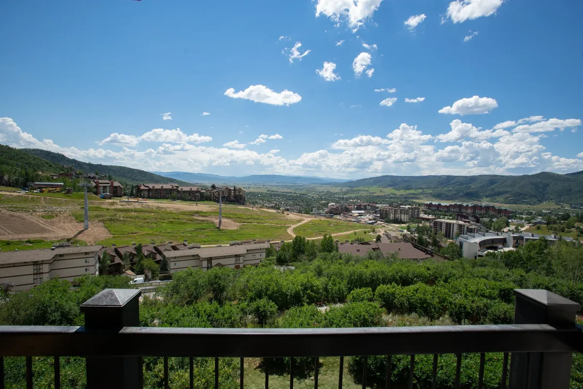 This image presents a sweeping view of a mountain range under a dynamic sky, with the town of Steamboat Springs nestled below and lush greenery in the foreground. The perspective suggests proximity to both natural beauty and the vibrant local community, capturing the transition from outdoor adventure to downtown exploration.